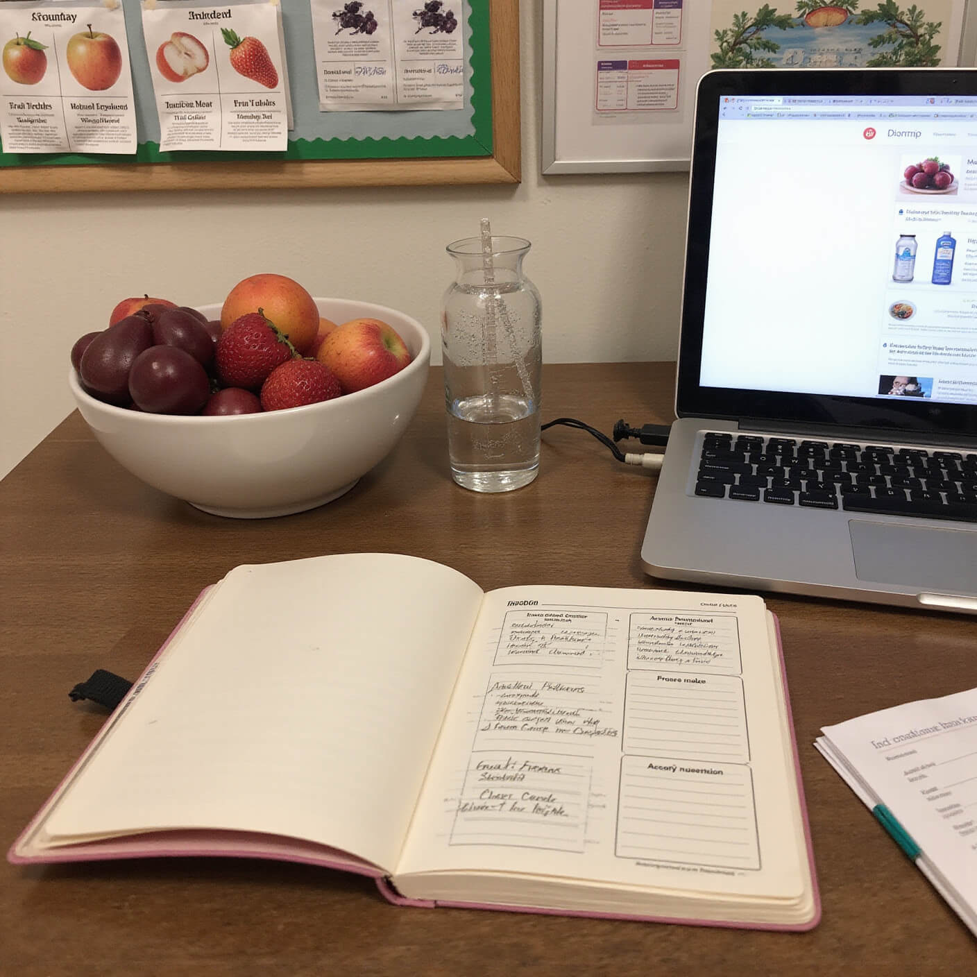 Home office wellness corner with open journal tracking fruit intake, fresh fruit bowl, hydration station, laptop showing nutrition research, and pinboard with seasonal fruit charts, bathed in warm afternoon light.